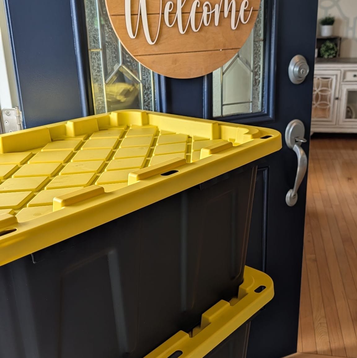 Close-up of a bright yellow lid resting on a black Crate & Key moving tote at a navy front door.