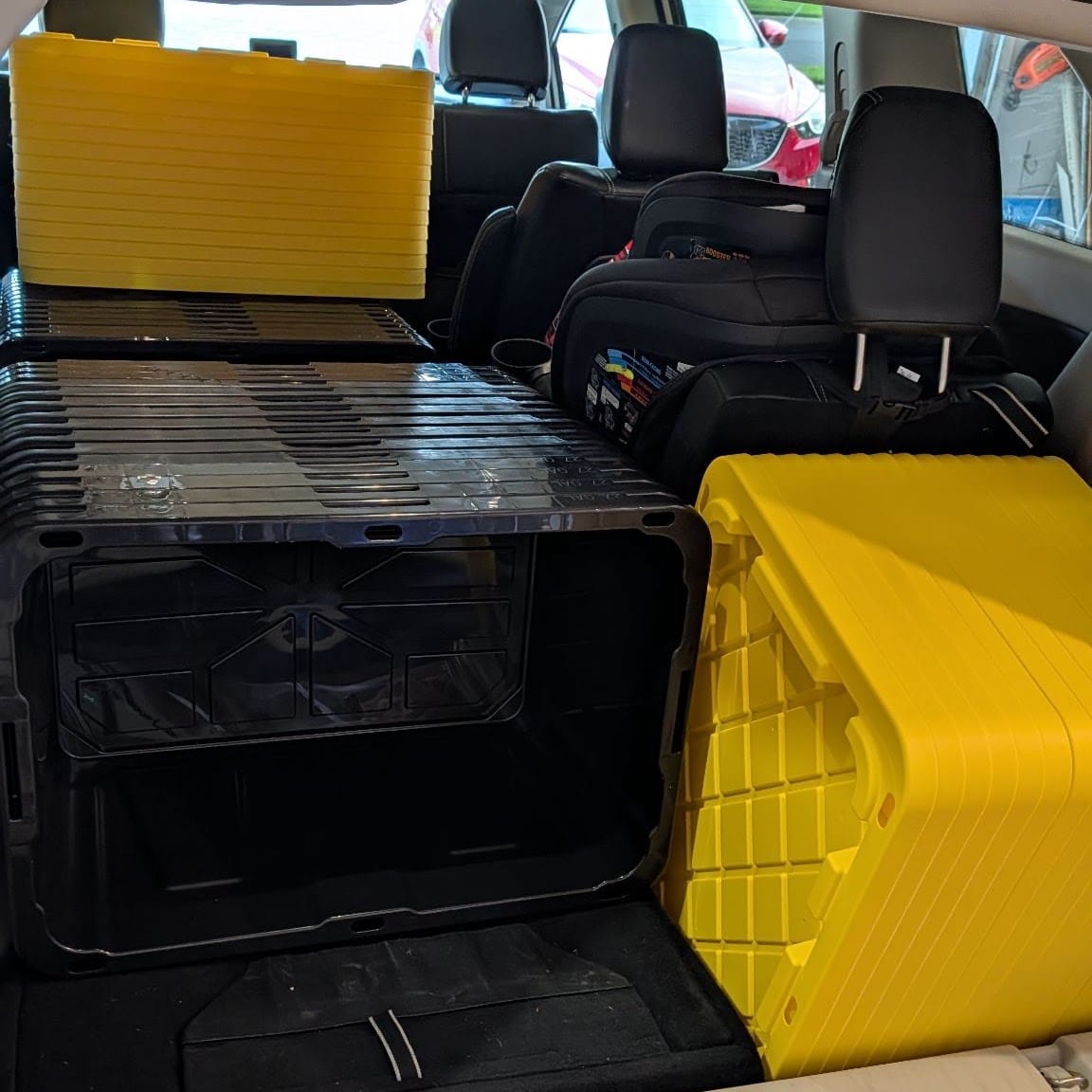 Black and yellow Crate & Key totes loaded flat in an SUV cargo area next to child car seats, ready to be delivered.